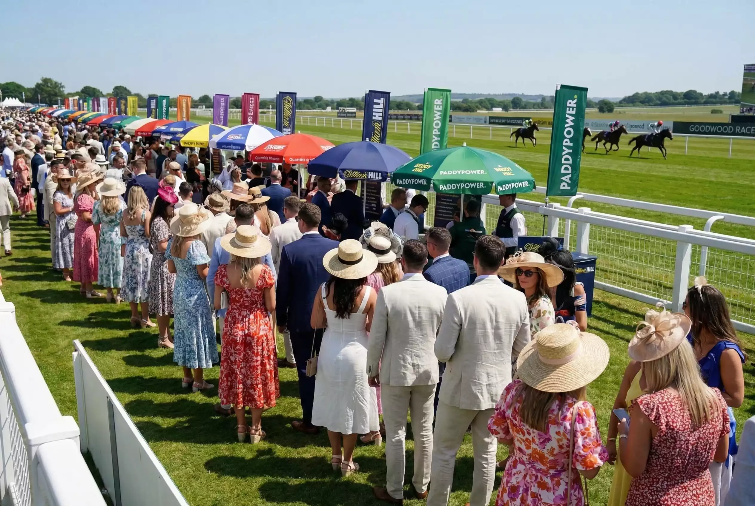 Racegoers queuing at the betting ring at Goodwood on a busy festival day with promotional banners visible